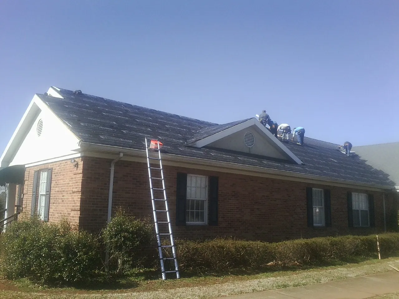 Crew tearing shingles off a brick ranch roof with a ladder set — Metal Roof Repair work by our crew in Low Moor