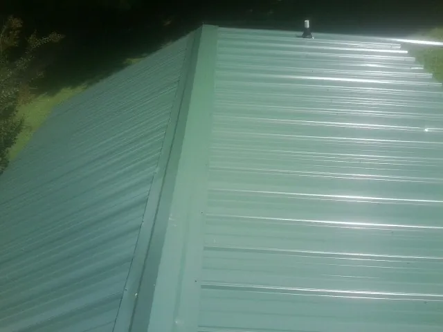 New green metal panels meeting at the ridge of a roof — Flat Roof Repair work by our crew in Low Moor