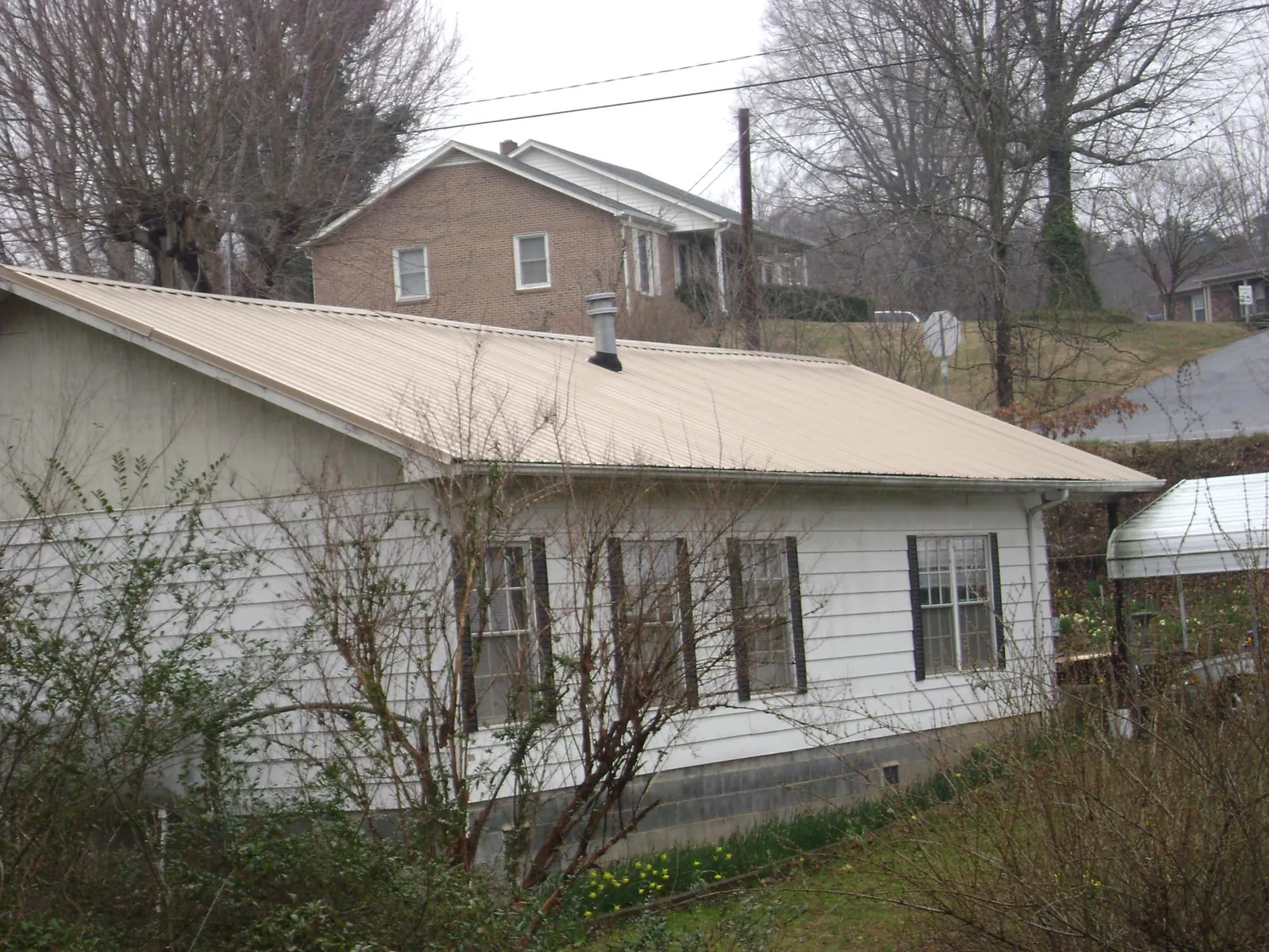 Tan metal roof on a white sided house set into a hillside — Commercial Roofing by Roofing Brothers in Low Moor